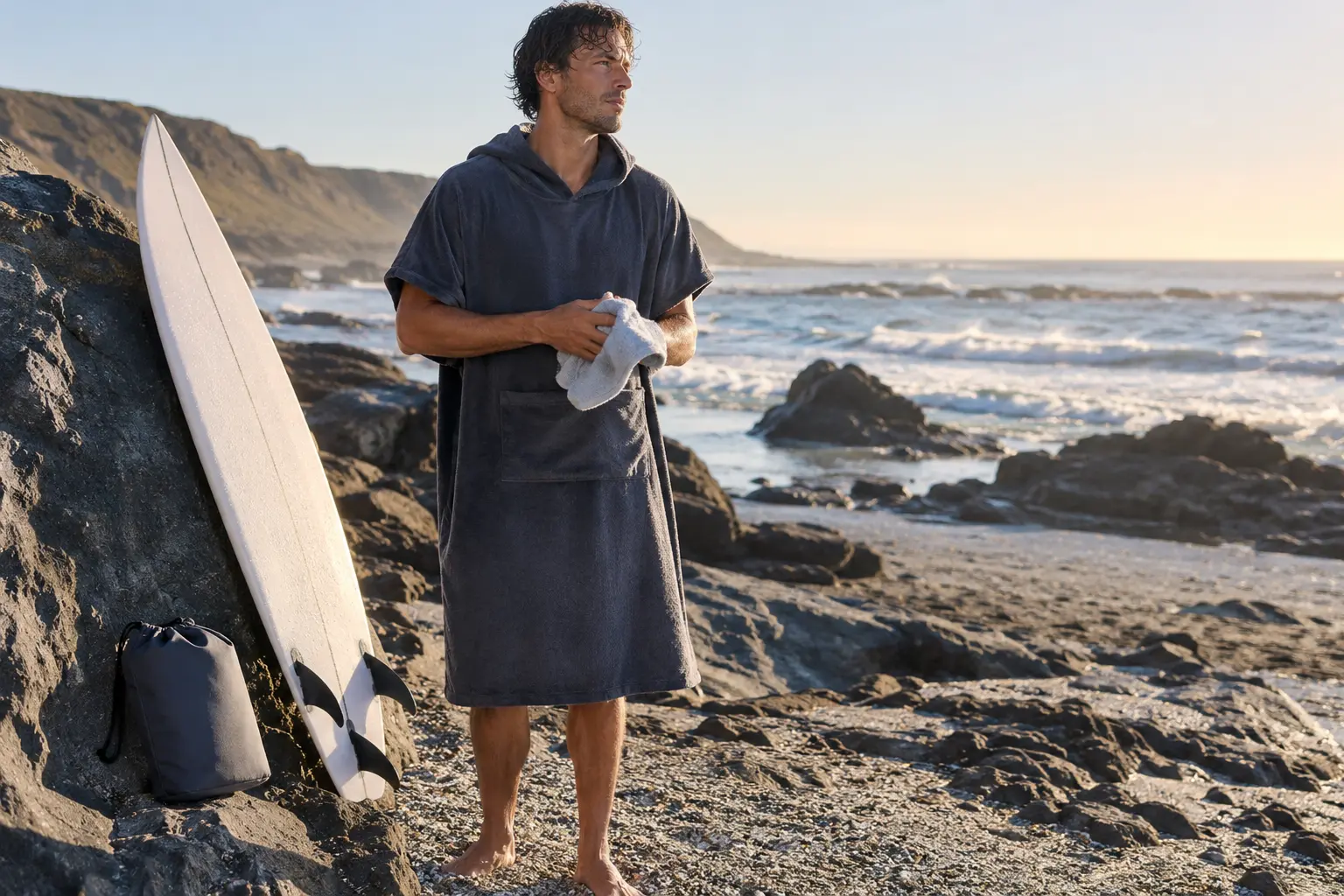 Surfeur portant un poncho en microfibre près de sa planche et d’un sac compact